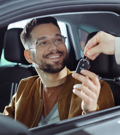 Hombre con gafas recibiendo las llaves a través de la ventana del asiento del conductor.
